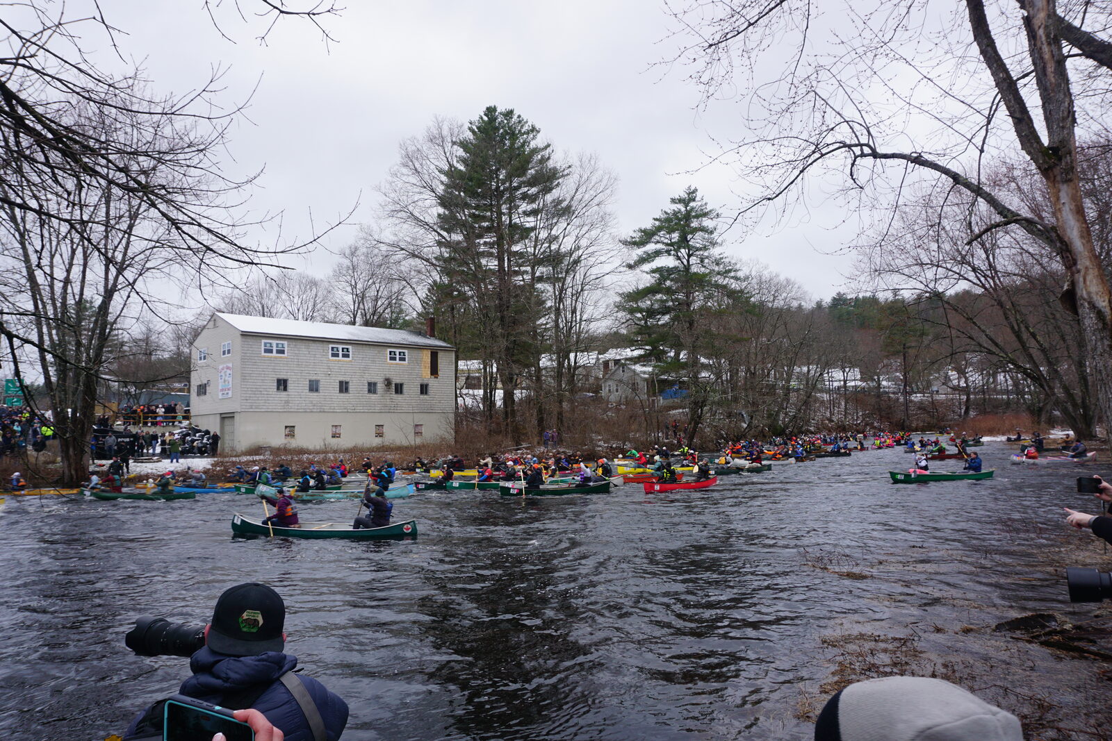 Canoes lined up on the river at the start of the race, with spectators gathered along the bank