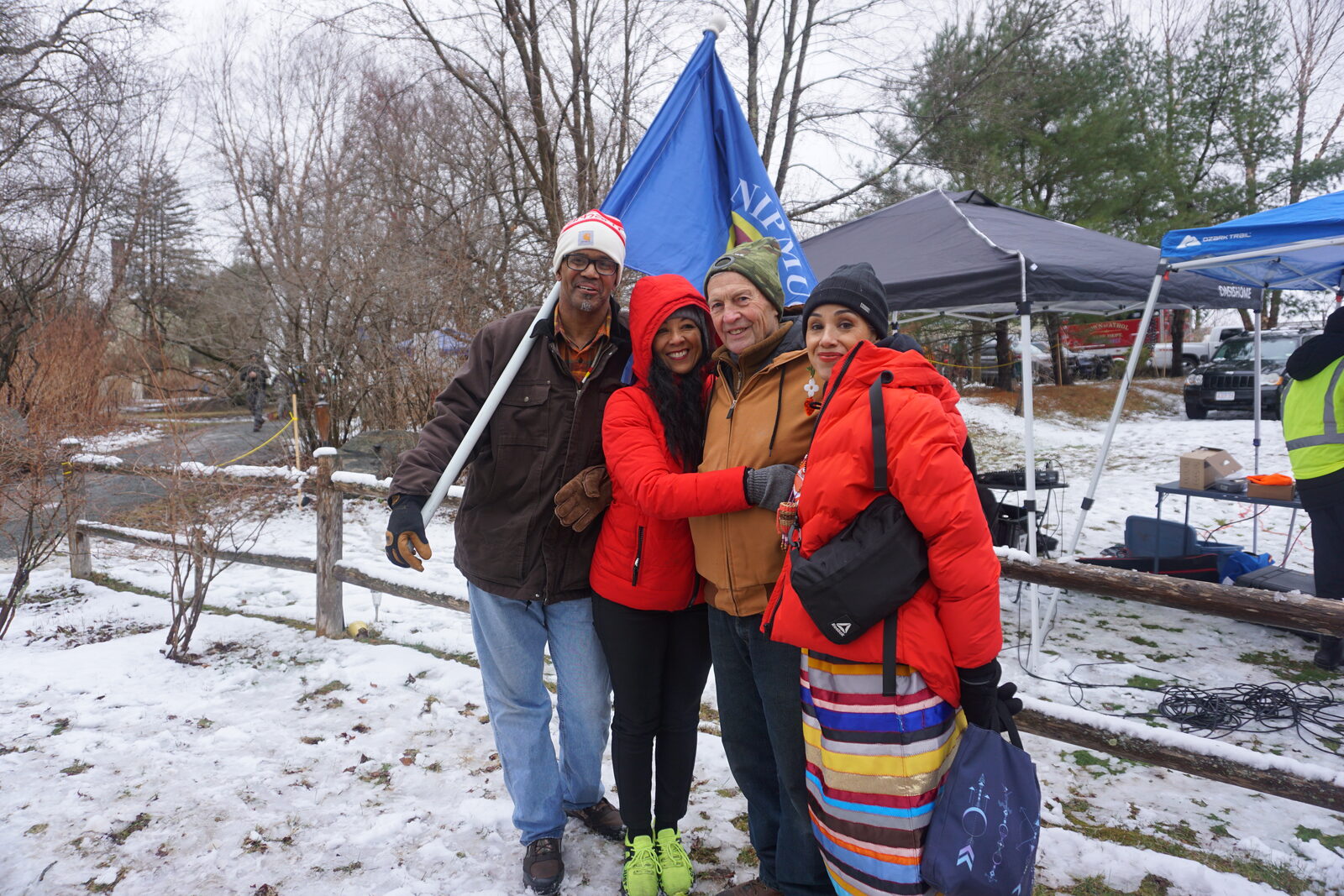 Community members posing with the Nipmuc Nation flag beside the river