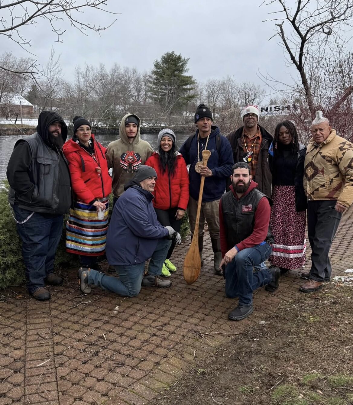 Group portrait of community members with a carved canoe paddle beside the river