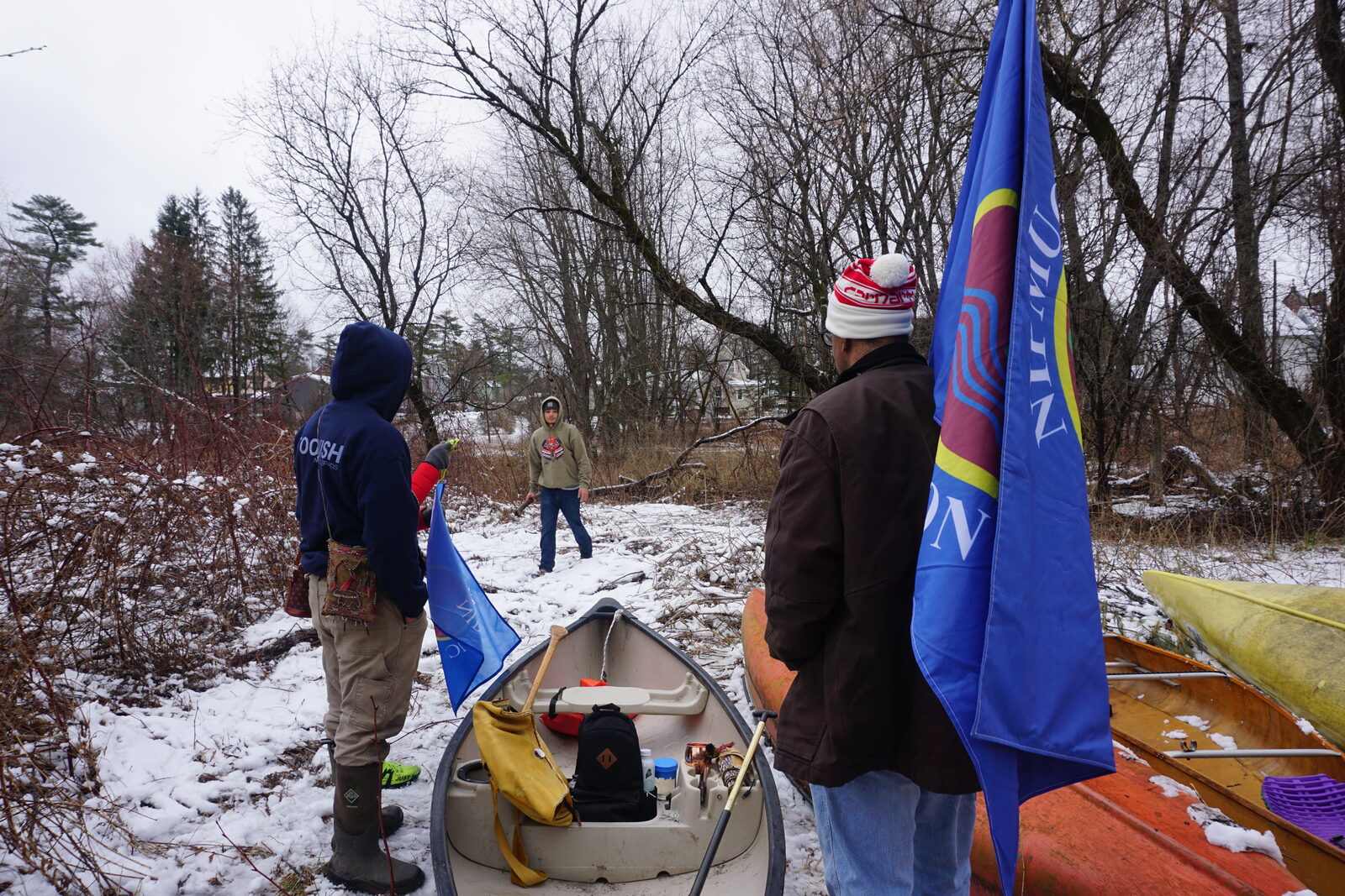 Community members preparing a canoe and flag for launch on a snowy riverbank