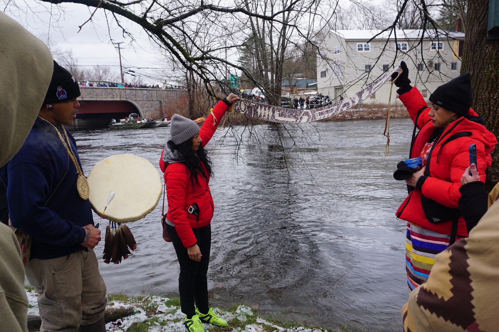 Community members holding up a wampum belt near the river, with a hand drum nearby