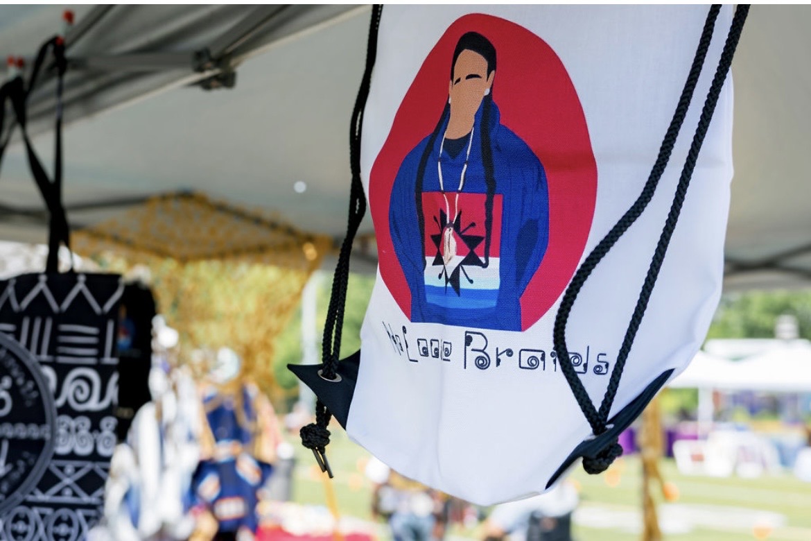 A No Loose Braids drawstring bag hanging at a vendor tent
