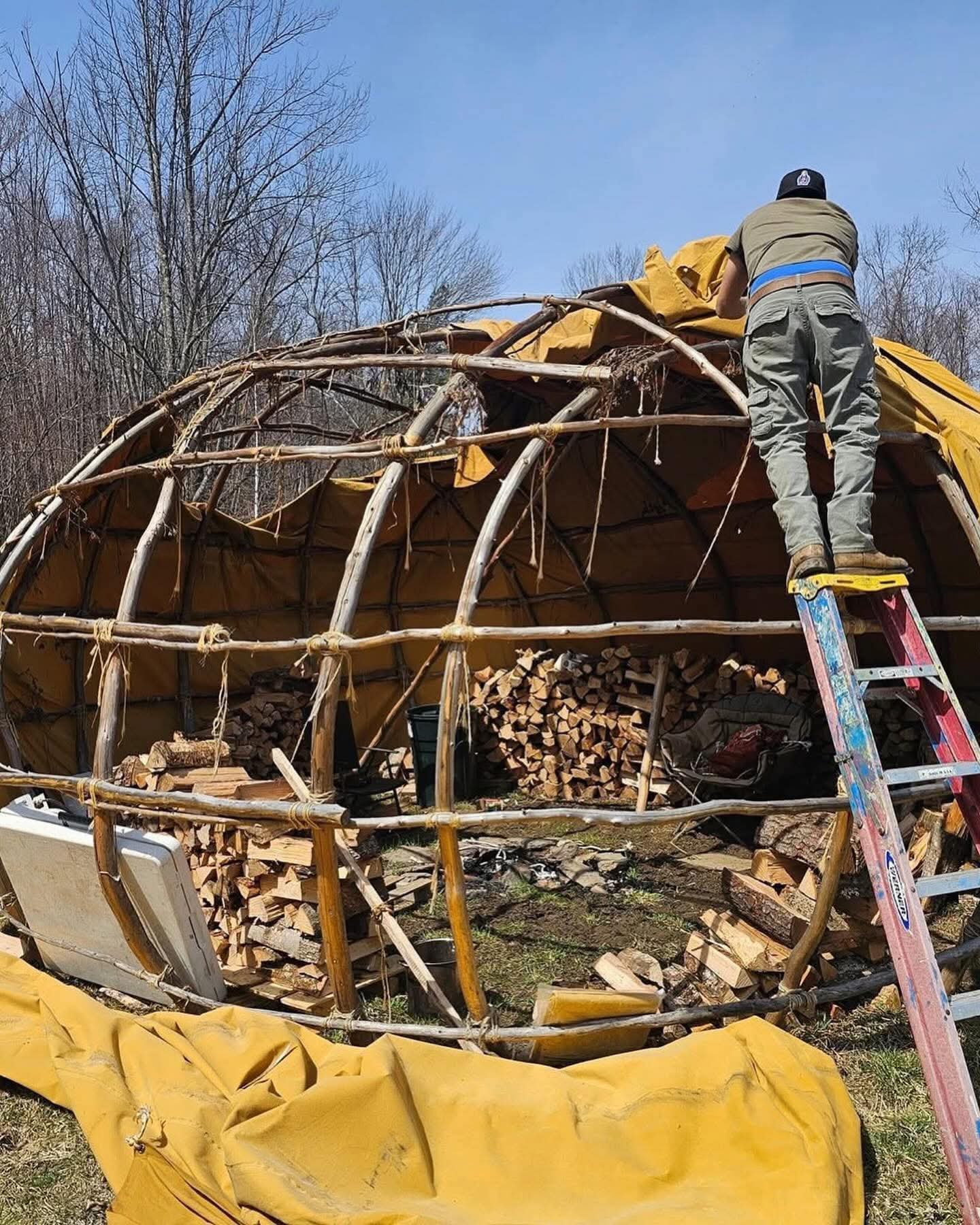 A man on a ladder helping build a large wigwam frame