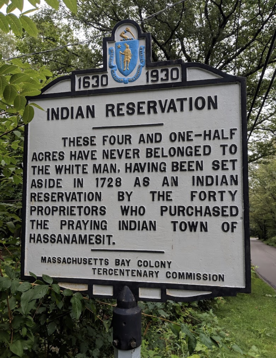 Massachusetts Bay Colony Tercentenary Commission historical marker reading: Indian Reservation. These four and one-half acres have never belonged to the white man, having been set aside in 1728 as an Indian reservation by the forty proprietors who purchased the praying Indian town of Hassanamesit.