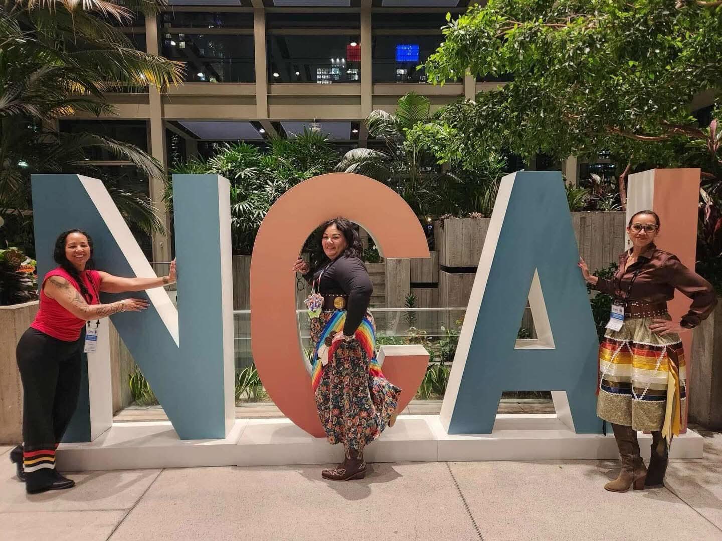 Three women posing at a large NCAI conference sign