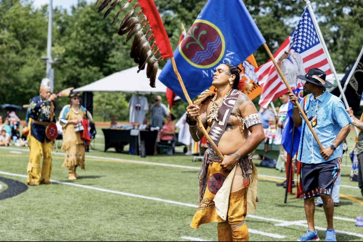 A flag bearer carrying the Nipmuc Nation flag alongside the American flag at the powwow