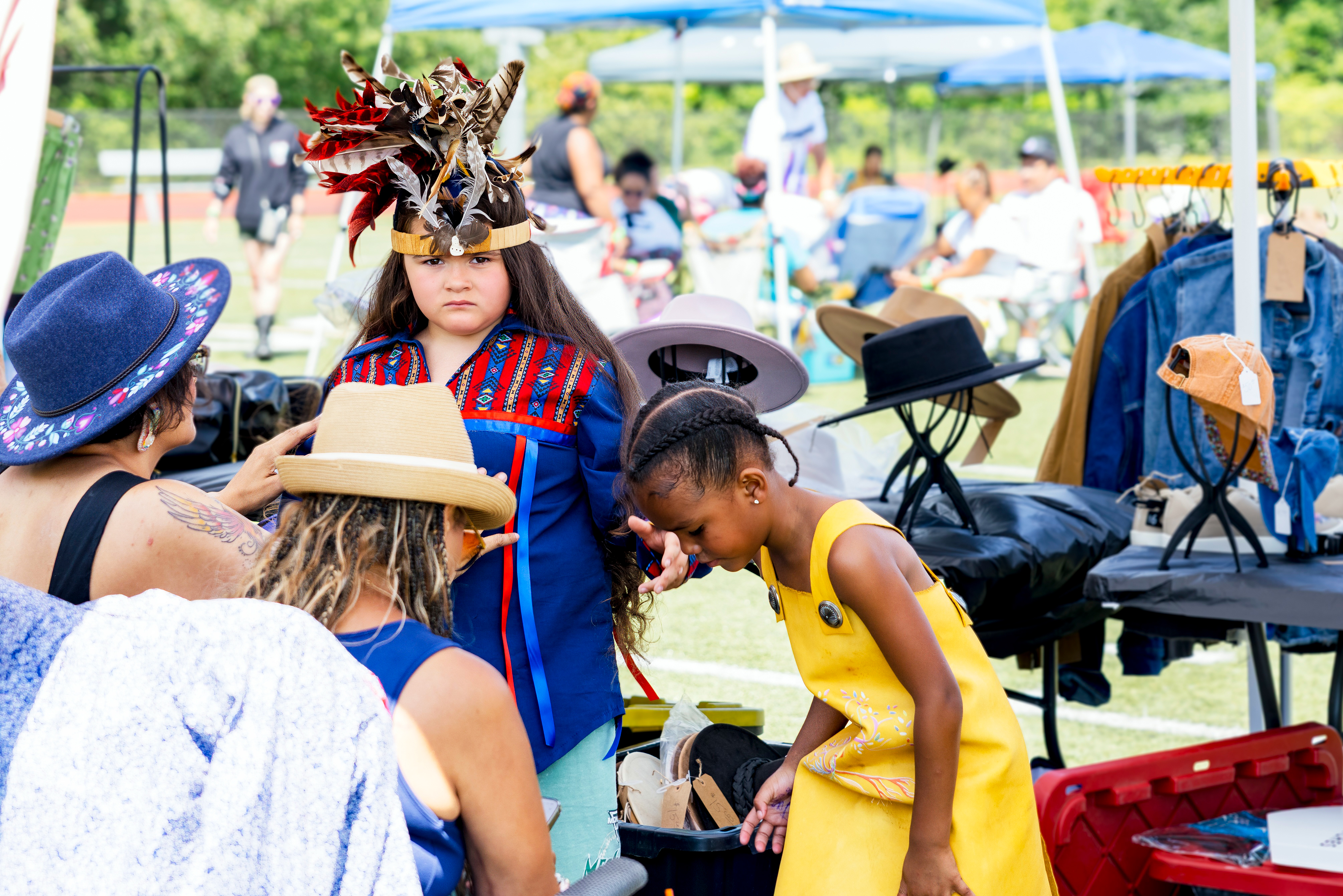 A young dancer in a feathered headdress with community members at the powwow