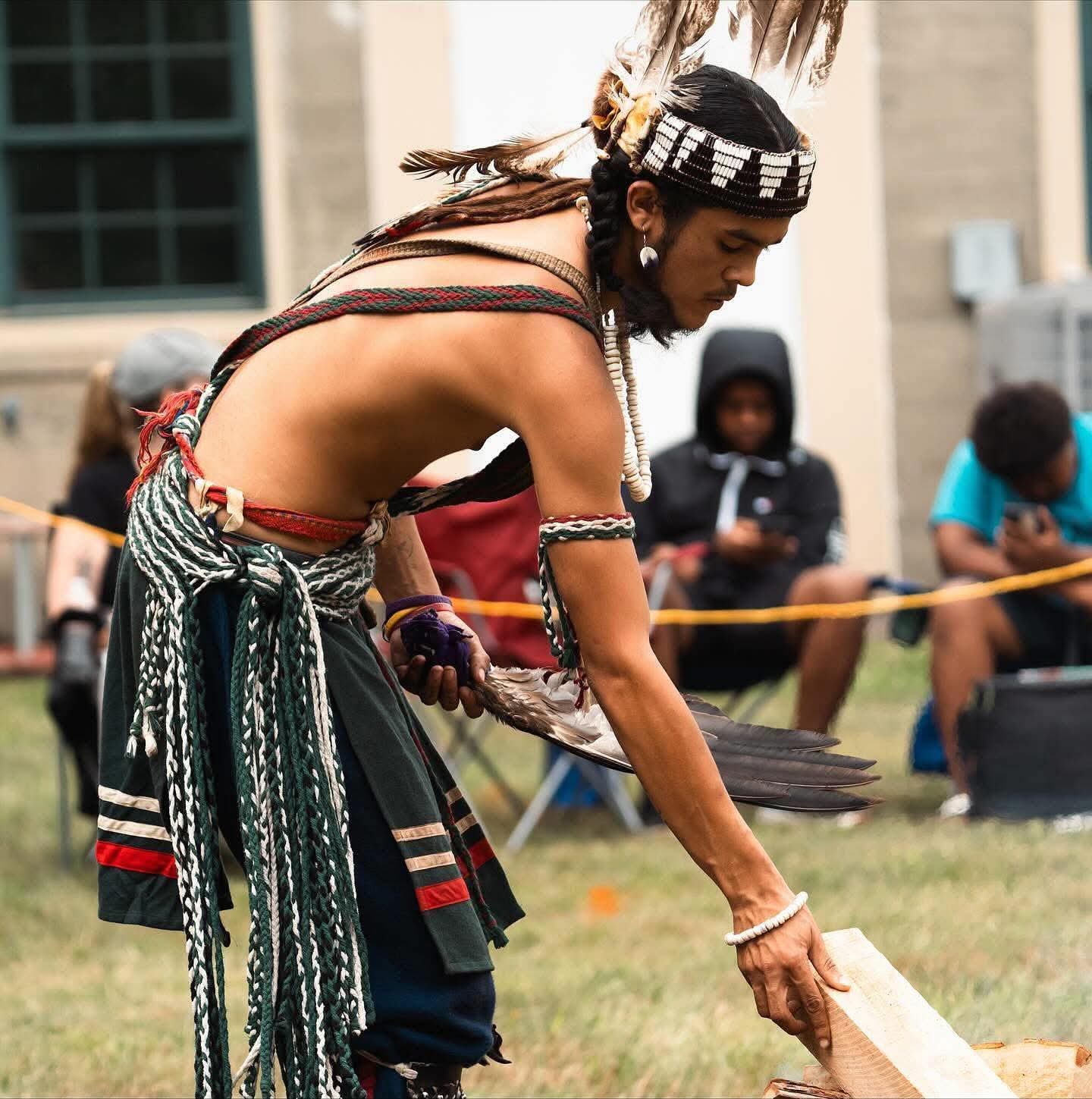 Dancer in regalia with an eagle feather fan tending the ceremonial fire