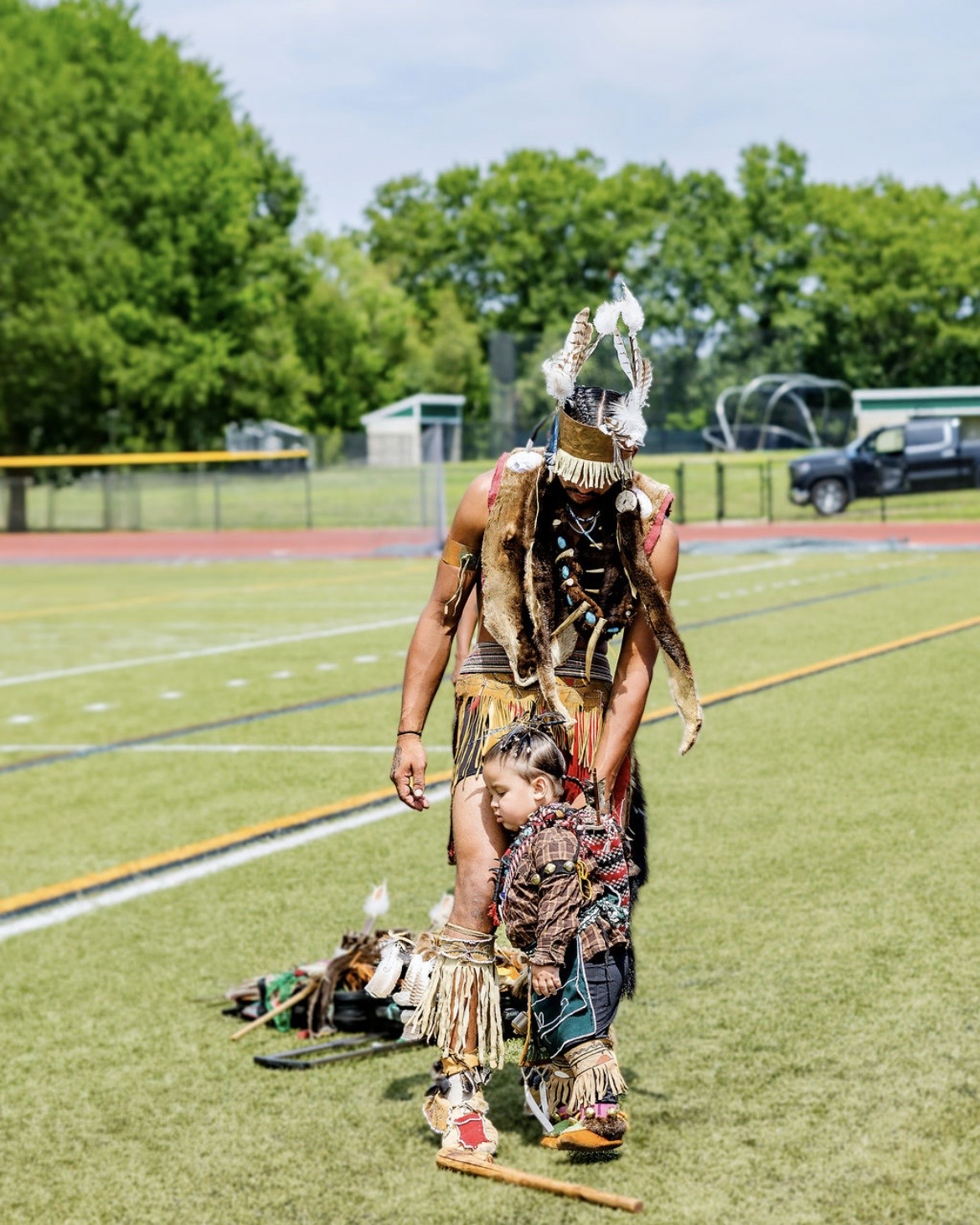 A man in regalia walking with a toddler at the powwow