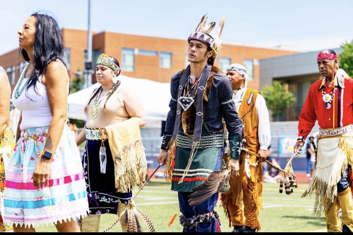 Community members in regalia leading the powwow procession