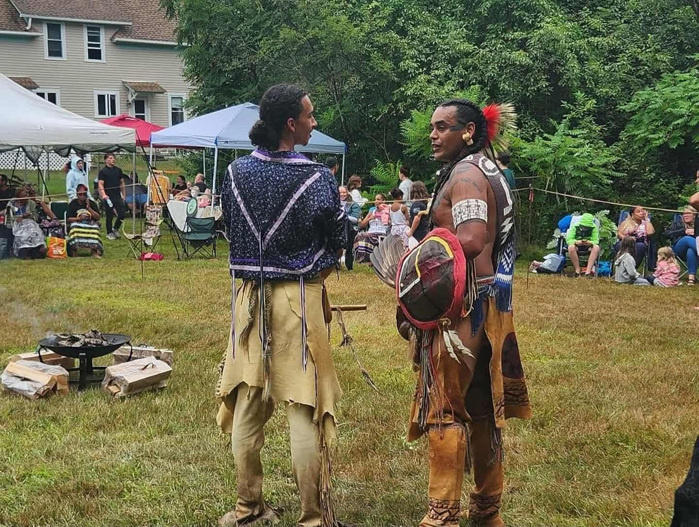 Two dancers in regalia speaking beside the fire pit at the powwow