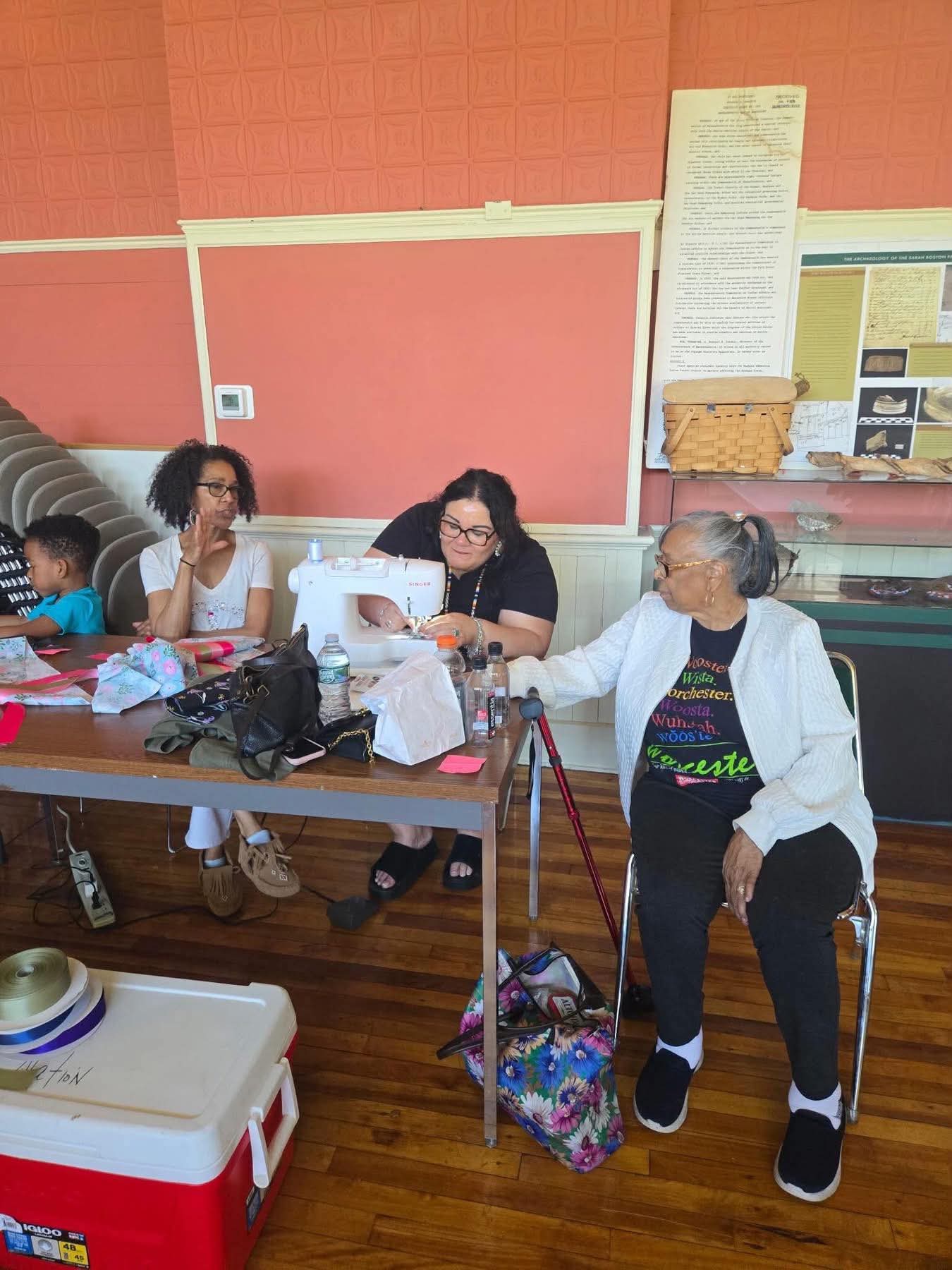 Community members gathered around a sewing machine during the ribbon skirt workshop