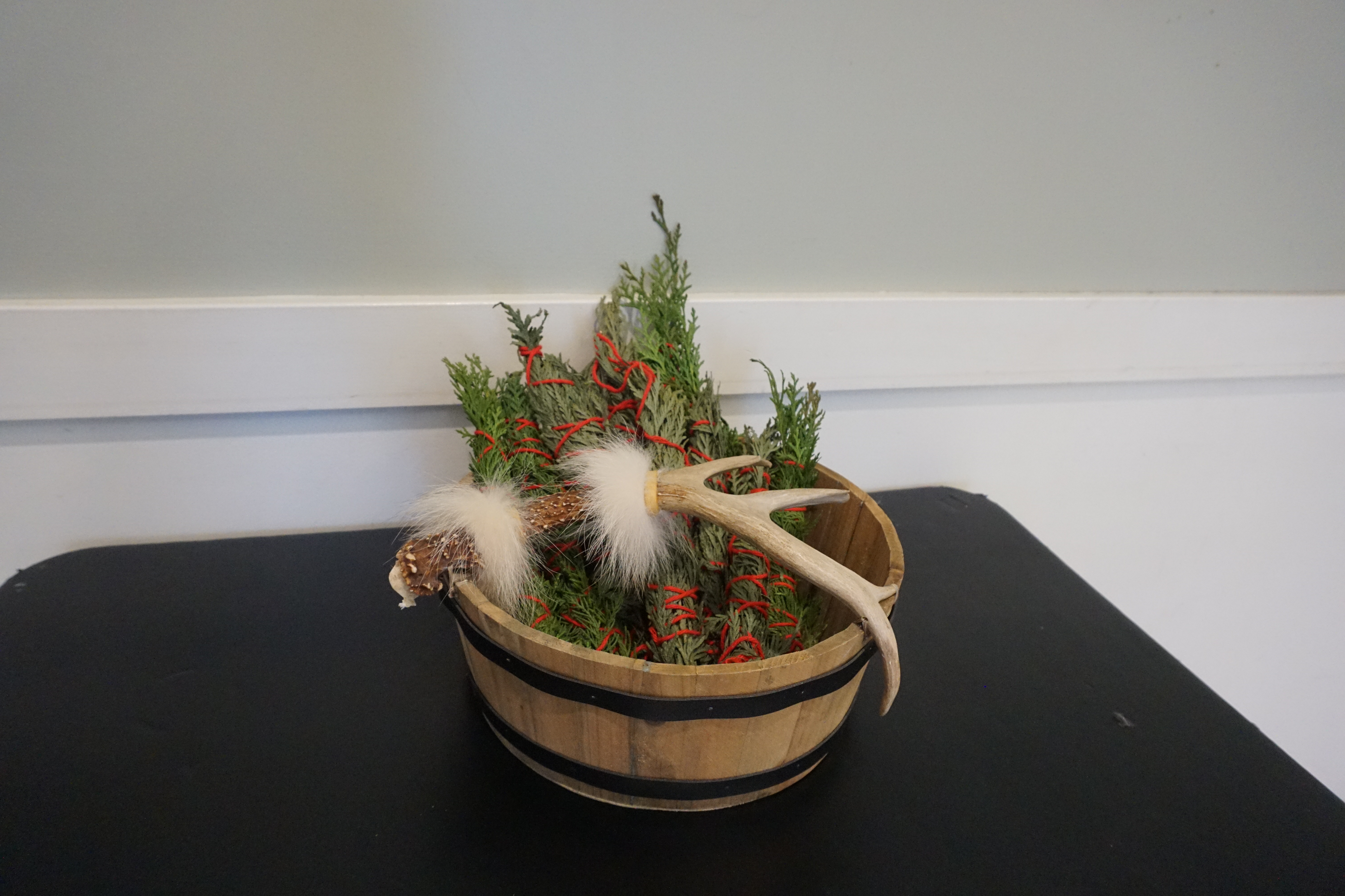 A basket of cedar bundles, an antler, and feathers displayed at the Trade Event