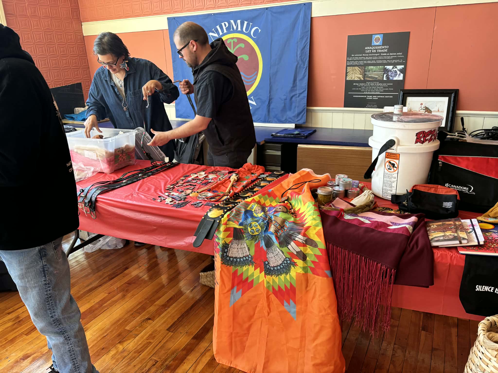 Vendor table with handmade jewelry, regalia pieces, and a Nipmuc Nation flag banner