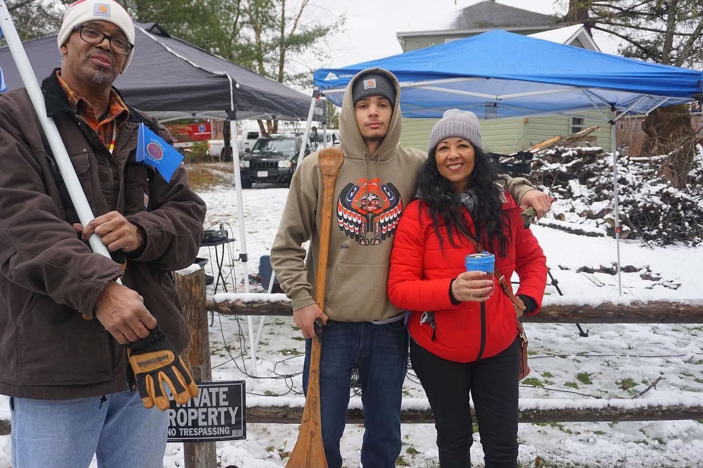 Community members with a carved canoe paddle at the water ceremony, snow on the ground